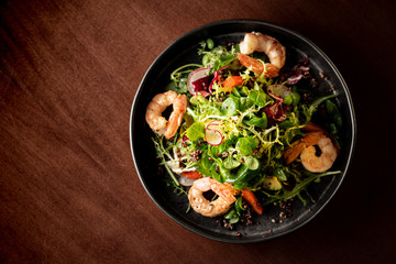 Shrimps salad with cherry tomatoes, cucumeber, avocado, lettuce and pomegranate on dish. Healthy seafood concept. Tasty grilled prawn shrimp and mix vegetable salad on black wood