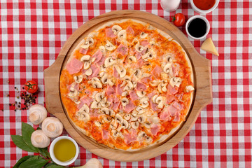 Rustic pizza with cheese, ham, sausage, mushrooms and tomatoes sauce, served on a wooden board for a dinner in italian restaurant background, top view. Classic Italy food. Close up