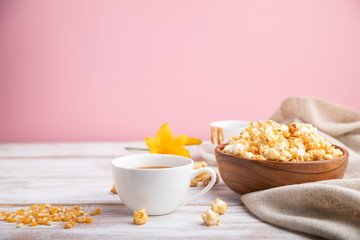 Popcorn with caramel in wooden bowl and a cup of coffee on a white and pink background. Side view, copy space, selective focus.