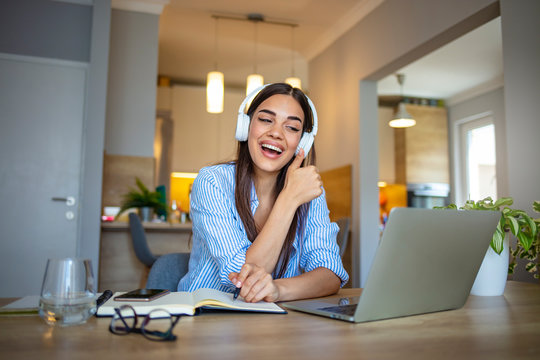Focused woman wearing headphones using laptop at home, writing notes, attractive female student learning language, watching online webinar, listening audio course, e-learning education concept