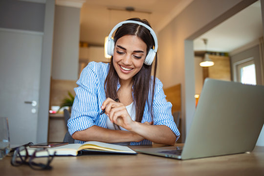 Focused young businesswoman or student looking at laptop holding book learning, serious woman working or studying with computer doing research or preparing for exam online