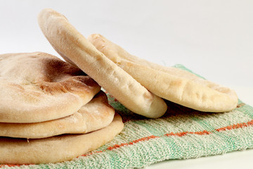freshly baked or fresh pita or arabic breads on a rustic cloth and a wooden board on a white surface