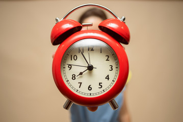 Woman is holding in hands a red alarm clock close up.