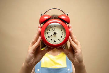 Woman is holding in hands a red alarm clock close up.