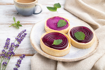 Sweet tartlets with jelly and milk cream with cup of coffee on a white wooden background. Side view.