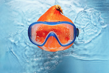 Orange pumpkin swimmer in a mask in blue water. Halloween concept