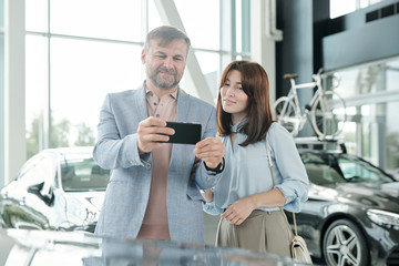 Obraz premium Happy mature man with smartphone taking photo of luxurious new car