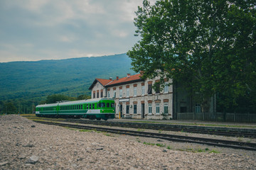 Older style diesel multiple unit DMU train in white and green color in green environment in non urban environment. Train in front of an older station.