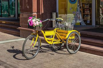 Fototapeta na wymiar Yellow tricycle with flowers in baskets, standing at the entrance to the store