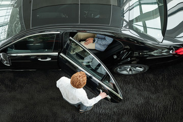 Sales manager closing the door of car with clients inside before test drive