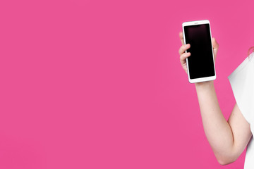 Fototapeta na wymiar Look at this cell phone. Contented happy woman, pointing her index finger at a blank screen, shows a modern device. Isolated on a pink background.