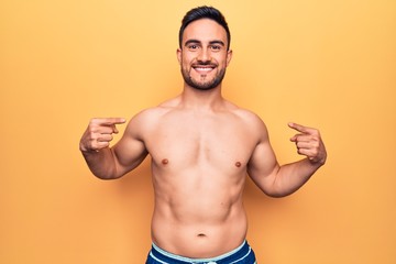 Young handsome man with beard wearing sleeveless t-shirt standing over yellow background looking confident with smile on face, pointing oneself with fingers proud and happy.