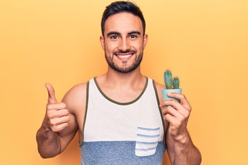Young handsome man with beard wearing sleeveless t-shirt holding cactus plant pot smiling happy and...