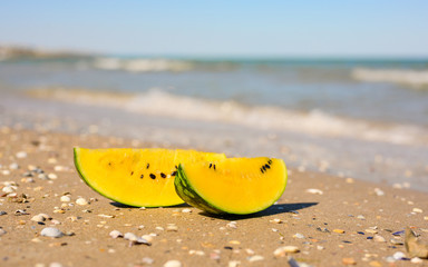 Fototapeta na wymiar Two slices of yellow watermelon stand on the beach. In the background the sea.