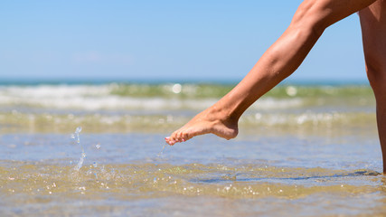 Girl's foot splashes sea water. Woman's leg on the background of the sea