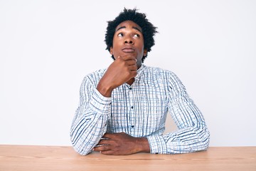 Handsome african american man with afro hair wearing casual clothes sitting on the table serious...