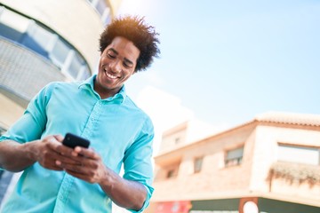 Young handsome african american man wearing casual clothes smiling happy. Standing with smile on face using smartphone at town street.