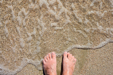 The sea wave on a sandy beach washes men's feet. Sea vacation concept.
