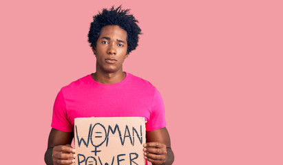 Handsome african american man with afro hair holding woman power banner thinking attitude and sober...