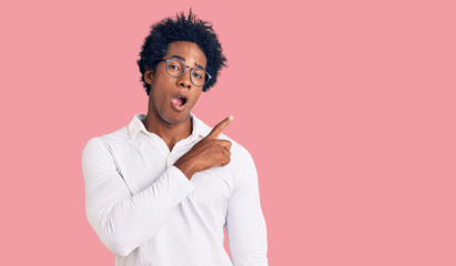 Handsome african american man with afro hair wearing casual clothes and glasses surprised pointing with finger to the side, open mouth amazed expression.