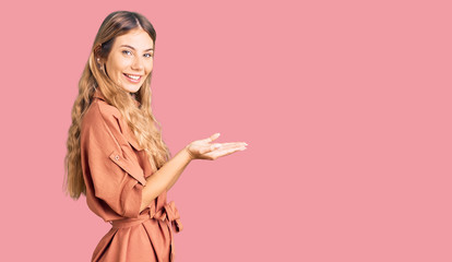 Beautiful caucasian woman with blonde hair wearing summer jumpsuit pointing aside with hands open palms showing copy space, presenting advertisement smiling excited happy