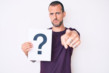 Fototapeta na wymiar Young handsome man with tattoo holding question mark pointing with finger to the camera and to you, confident gesture looking serious