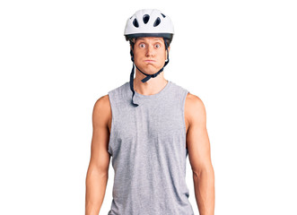 Young handsome man wearing bike helmet puffing cheeks with funny face. mouth inflated with air, crazy expression.