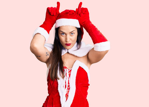 Young beautiful caucasian woman wearing santa claus costume doing funny gesture with finger over head as bull horns