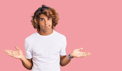 Young hispanic man wearing casual white tshirt clueless and confused with open arms, no idea...