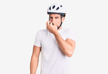 Young handsome man wearing bike helmet smelling something stinky and disgusting, intolerable smell,...