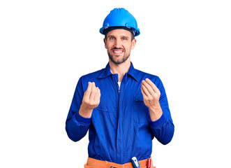Young handsome man wearing worker uniform and hardhat doing money gesture with hands, asking for salary payment, millionaire business
