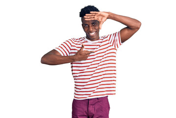 Naklejka premium Young african american man wearing casual clothes smiling making frame with hands and fingers with happy face. creativity and photography concept.