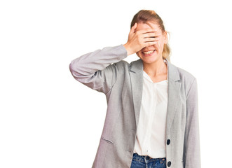 Young beautiful blonde woman wearing elegant jacket smiling and laughing with hand on face covering eyes for surprise. blind concept.