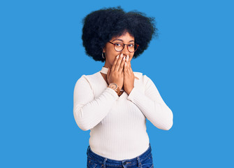 Young african american girl wearing casual clothes and glasses laughing and embarrassed giggle covering mouth with hands, gossip and scandal concept