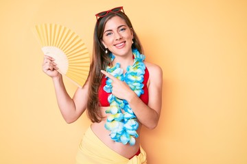 Beautiful young caucasian woman wearing summer look and holding hand fan smiling happy pointing with hand and finger