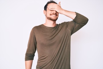 Young handsome man wearing casual clothes smiling and laughing with hand on face covering eyes for surprise. blind concept.