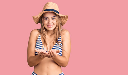 Young beautiful blonde woman wearing bikini and hat smiling with hands palms together receiving or giving gesture. hold and protection