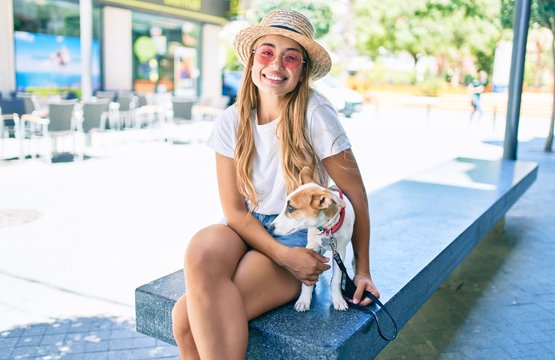 Young beautiful blonde woman walking the dog outside on a summer day sitting on a bench