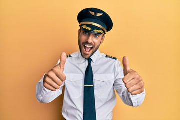 Handsome hispanic man wearing airplane pilot uniform approving doing positive gesture with hand, thumbs up smiling and happy for success. winner gesture.