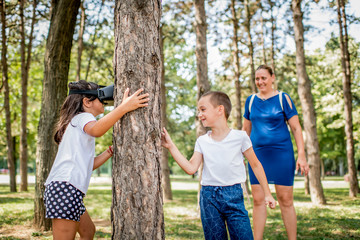 Fototapeta premium School children in white t shirts having fun with virtual reality headset outdoor in the park