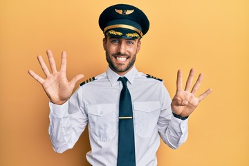 Handsome hispanic man wearing airplane pilot uniform showing and pointing up with fingers number nine while smiling confident and happy.