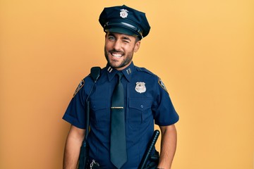 Handsome hispanic man wearing police uniform winking looking at the camera with sexy expression,...
