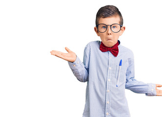 Cute blond kid wearing nerd bow tie and glasses clueless and confused expression with arms and hands raised. doubt concept.