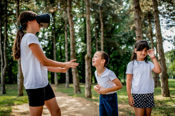 Obraz premium School children in white t shirts having fun with virtual reality headset outdoor in the park