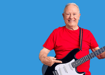 Senior handsome grey-haired man playing electric guitar smiling happy pointing with hand and finger