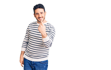 Fototapeta premium Young hispanic man wearing casual clothes beckoning come here gesture with hand inviting welcoming happy and smiling