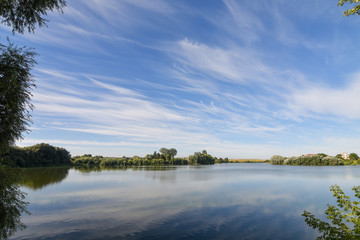 Beautiful summer landscape with lake and serene blue sky reflected in the water surface. Calm morning scenery