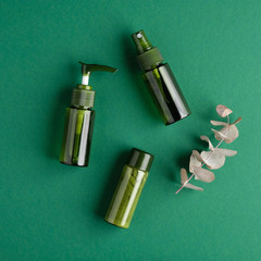 Green cosmetic bottles with eucalyptus leaf on green background. Natural organic beauty products, bio cosmetics, skin care concept