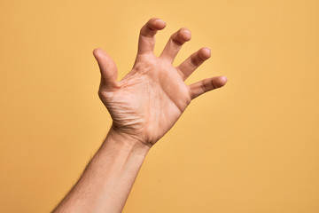 Naklejka premium Hand of caucasian young man showing fingers over isolated yellow background grasping aggressive and scary with fingers, violence and frustration