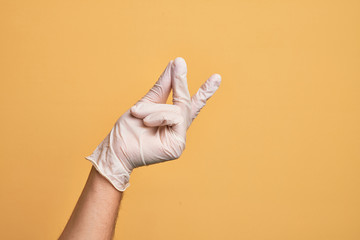 Hand of caucasian young man with medical glove over isolated yellow background snapping fingers for...